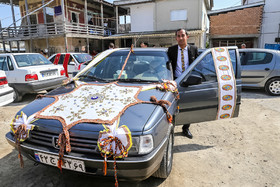 داماد در کنار ماشینی که برای مراسم تزیین شده است.