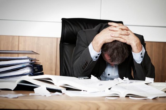 man-at-desk-surrounded-by-files-holding-his-head-in-his-hands.jpg