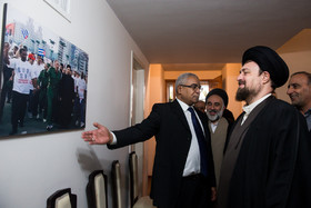 سید حسن خمینی در حال نگاه کردن به تصویر خود که سال ۱۳۸۰ همراه با فیدل کاسترو در کوبا نشان میدهد.