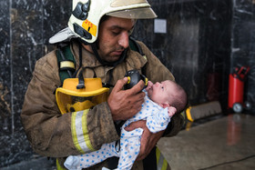یکی از نیروهای آتش نشان از طریق ماسک اکسیژن خود به نوزادی که از آتش سوزی نجات یافته اکسیژن میرساند