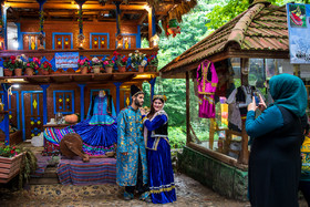 یک زوج گردشگر در حال تهیه عکس یادگاری با لباس‌های محلی گیلان در جلوی کلبه چوبی تزیین شده