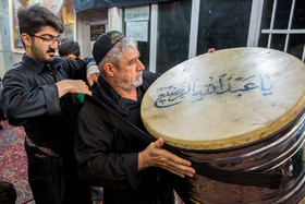 محمد حسن یکی از فرزندان ابوعبدالزهرا در حال کمک کردن به پدر برای مهار طبل بر گردن و آماده شدن مراسم عزاداری است.
