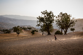 فوتبال بازی کردن یکی از کودکان روستای دلی در زمین های کشاورزی