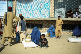 زنان سرپرست خانواده پس از دریافت سبد غذایی شان از طرف سازمان جهانی غذا در انتظار کمک برای جابجایی کیسههای آردی که تحویل گرفتهاند هستند.