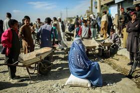 زنان سرپرست خانواده پس از دریافت سبد غذایی شان از طرف سازمان جهانی غذا در انتظار کمک برای جابجایی کیسههای آردی که تحویل گرفتهاند هستند.