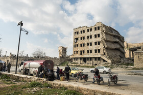 ویرانه‌ای باقی مانده از یکسری مجموعه ساختمان‌های دولتی شهر حلب که مردم بومی برای خرید مازوت، در این منطقه صف کشیده‌اند.
