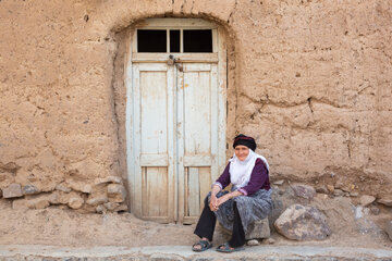 یکی از ساکنان روستای برزنون در مقابل خانه‌اش با دیوارهای خشتی در فصل تابستان.