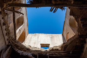 دورنمای آسمان آبی بندر بوشهر از درون سقف فروریخته‌ی عمارت «هفت بنگله» پیدا است.