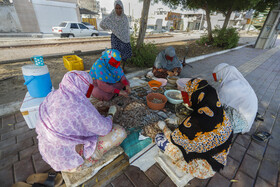 زنان در محله خواجه عطا بندرعباس در کنار خیابان مشغول پاک کردن میگو های صید شده از دریا هستند.
