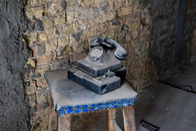 روبروی صندلی، در سمت مقابل، یک تلفن مشکی قدیمی سکه ای خاک گرفته وجود دارد که چند سالی است زنگ نخورده و هیچ کس گوشی آن را برنداشته است.